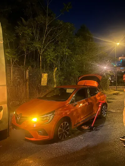 Gece yol kenarında turuncu hatchback aracın lastik değişimi