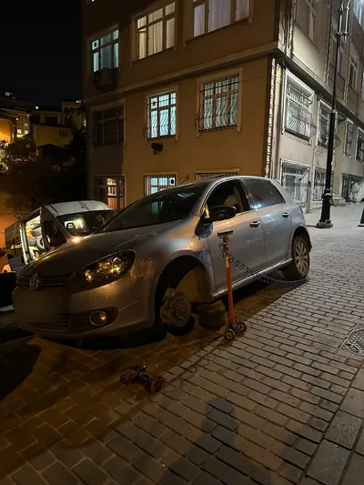 Gece arnavut kaldırımlı sokakta hatchback aracın ön tekeri sökülmüş hâlde
